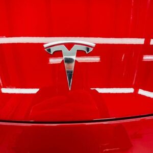 Red tesla paint covered in paint protection film underneath a Tesla badge