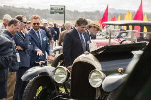 Bystanders at a car show gazing upon a beautiful black classic car in gloss black